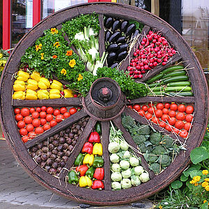 Altes Holzwagenrad mit frischem Gemüse und Blumen dekoriert
